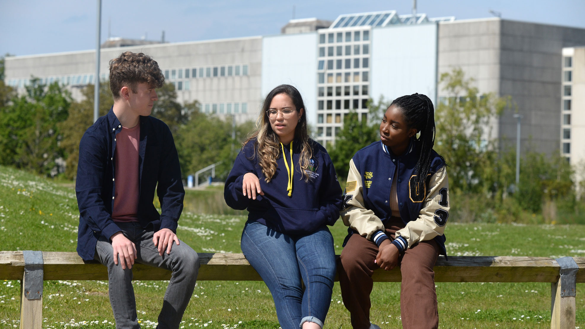 Three students sitting on front of the College building