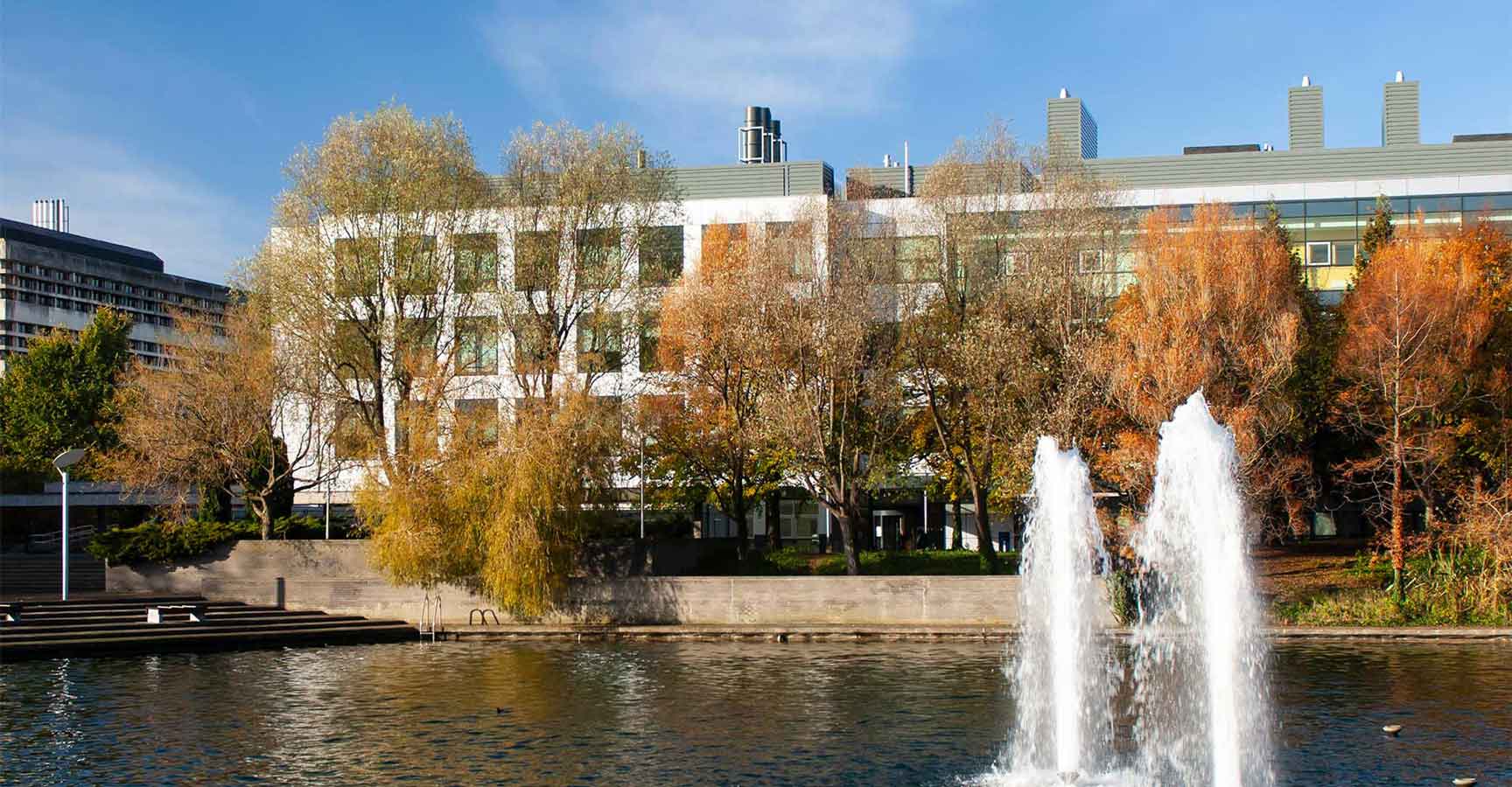 An image of two fountains in the UCD main lake surrounded by autumnal trees. The O'Brien Centre for Science can be seen through the trees.